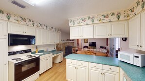 Una cocina con armarios blancos, una estufa, un microondas y un comedor con mesa y sillas.