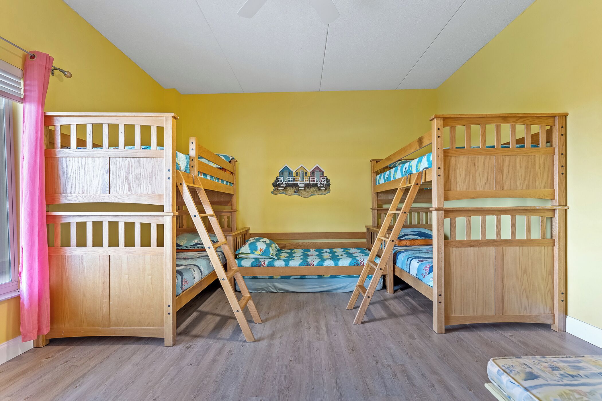 Una habitación con tres literas, una ventana con cortinas rosadas y un adorno en la pared.