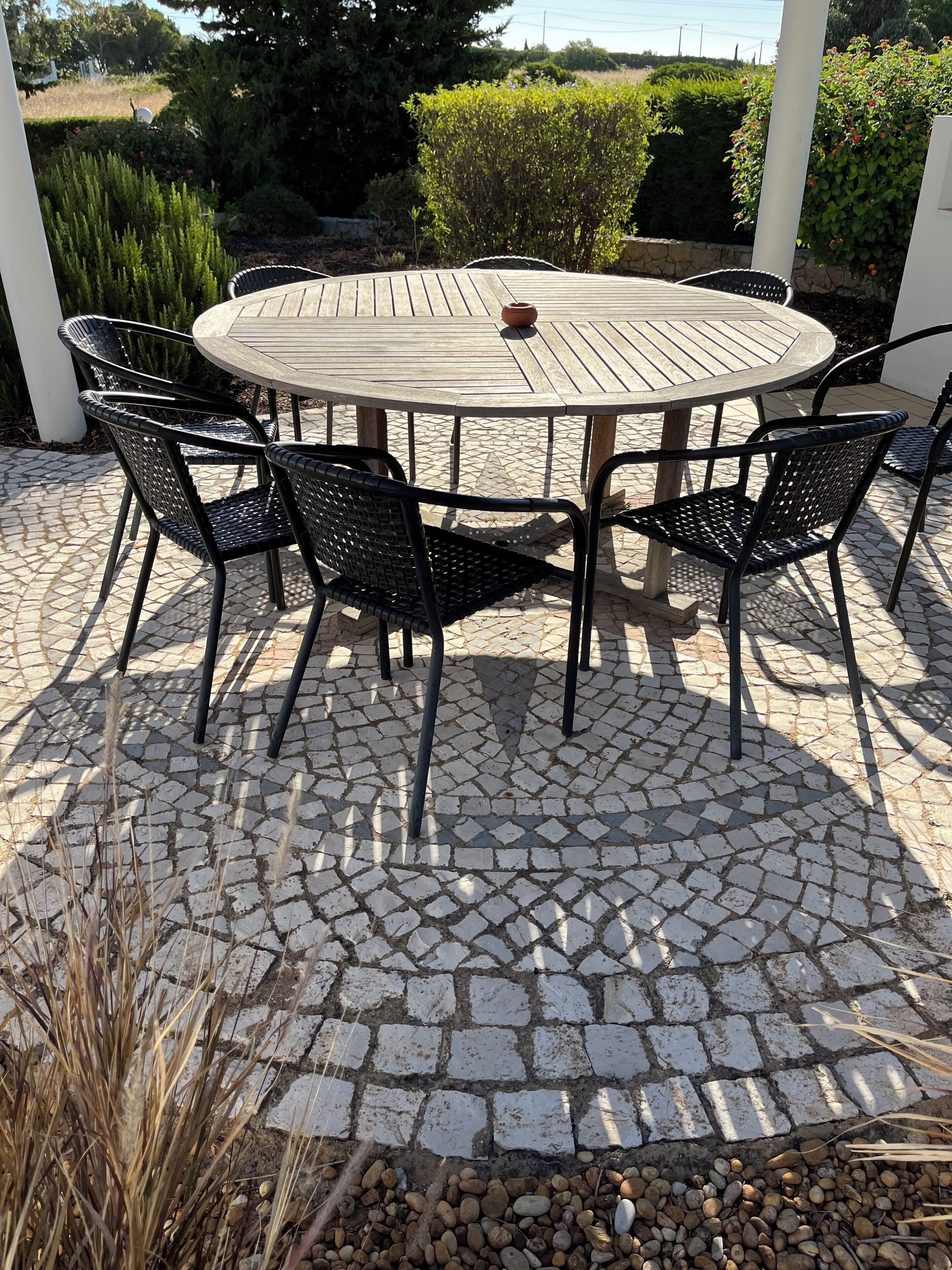 Una mesa redonda de madera con seis sillas negras de metal, rodeada por un patio con mosaicos.