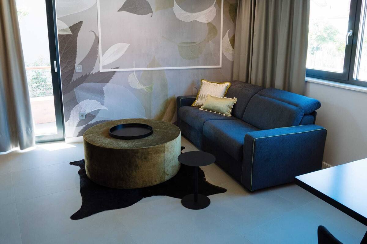 A modern living room with a blue sofa, a round ottoman, and a small table.