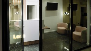 A modern hotel lobby with a glass entrance, a flat-screen TV mounted on the wall, and two plush armchairs. - Lena Luxury Apartments (Zadar)