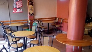 Interno di un ristorante con tavoli e sedie rotonde, pavimento a scacchi e un'ampia colonna.