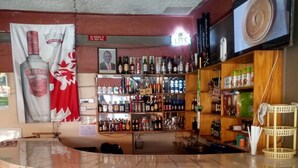 Angolo bar con un bancone piastrellato, due sgabelli e diverse bottiglie di liquore sugli scaffali.