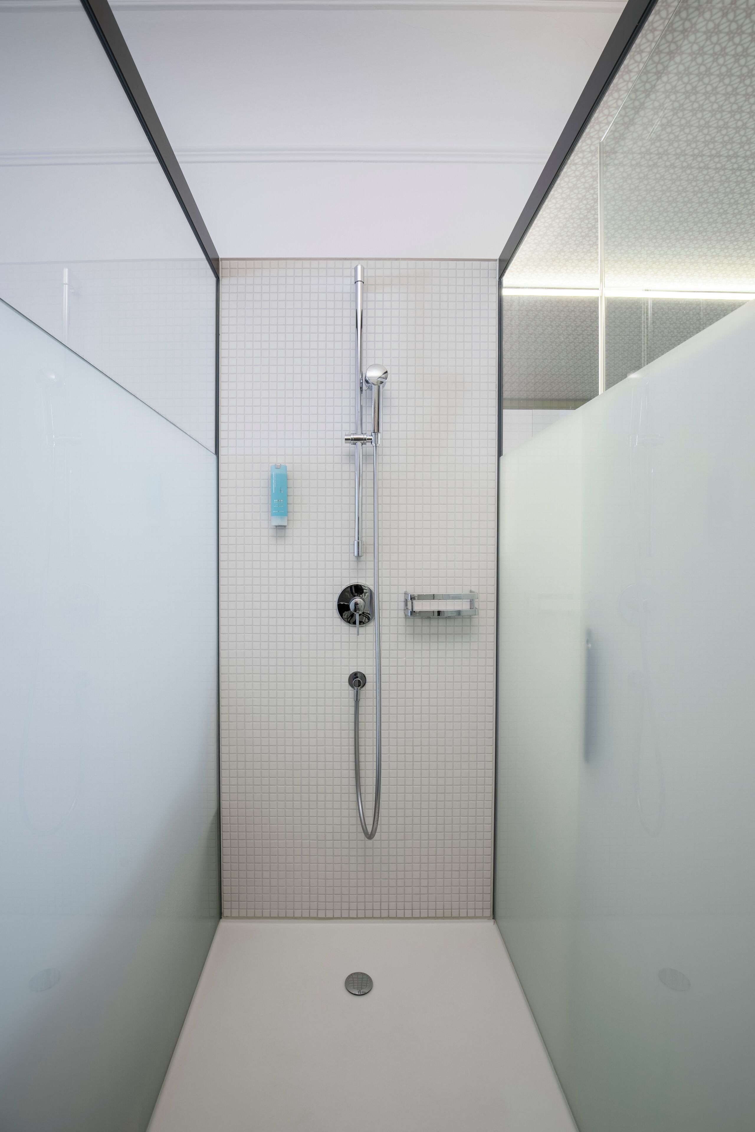 A modern shower with a grid-patterned wall, a handheld showerhead, and a wall-mounted faucet.