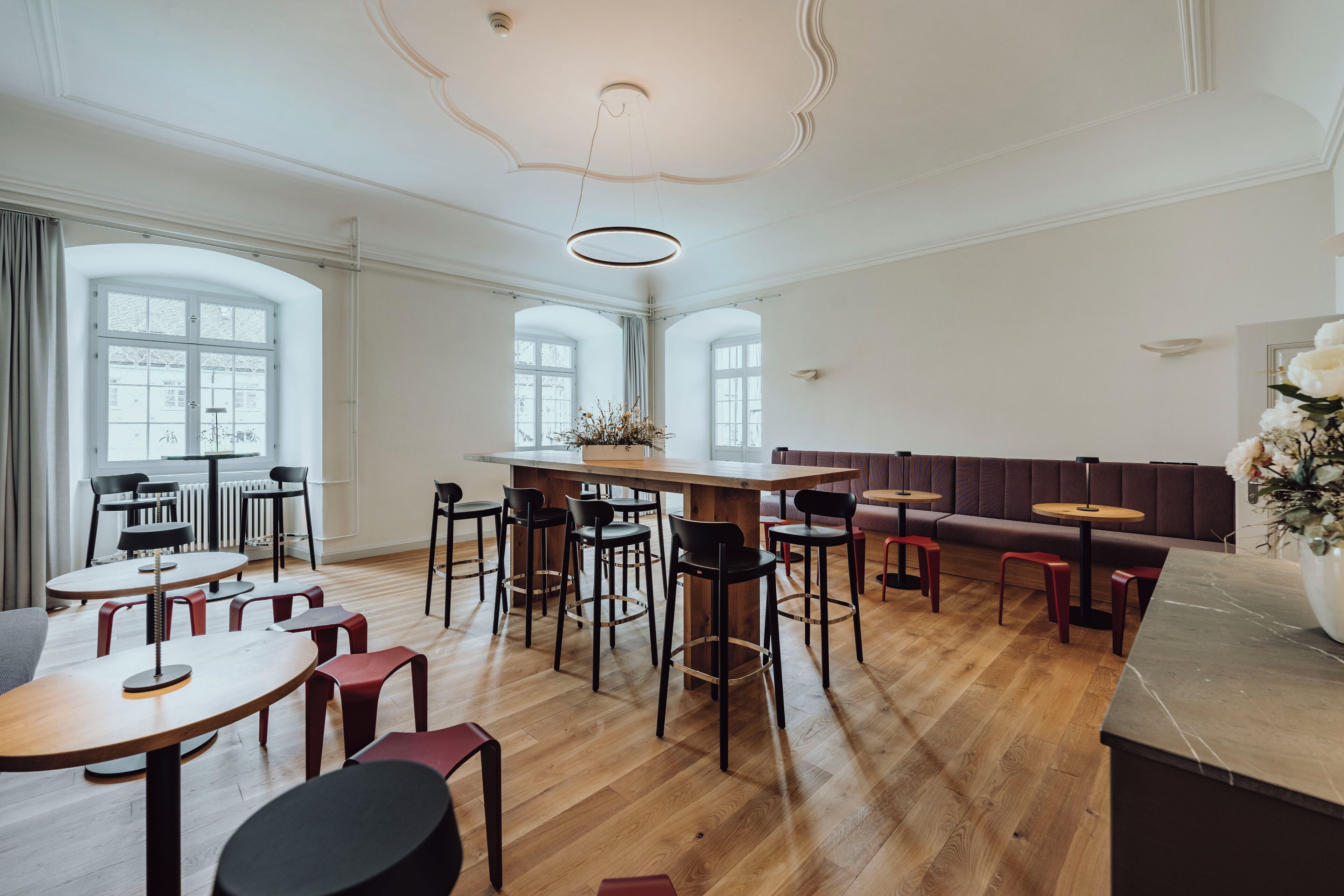 A spacious dining area with high ceilings, large windows, and a variety of seating options including tables and benches.