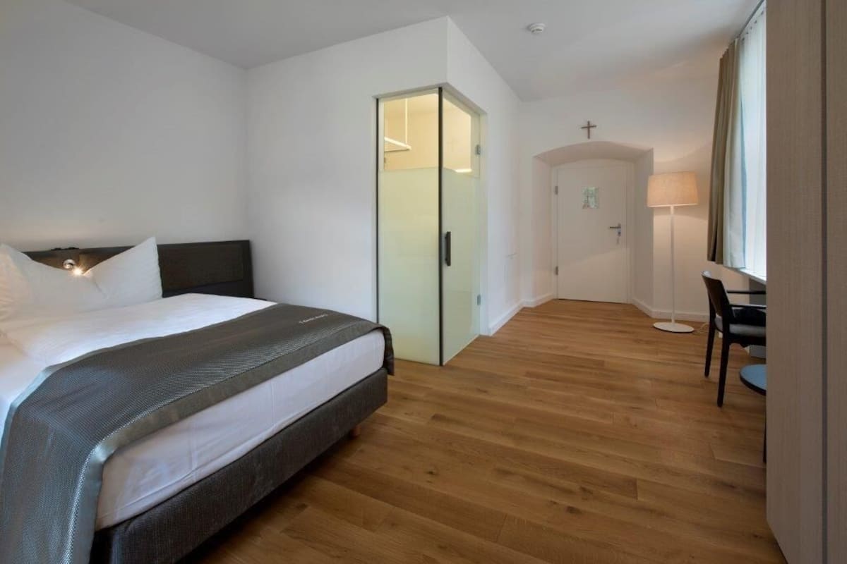 A hotel room with a bed, a desk, a chair, a wardrobe, and a mirror.