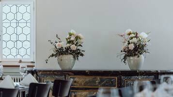 Een eetruimte met een lange tafel gedekt voor een maaltijd, twee vazen met bloemen en een raam met een honingraatpatroon.