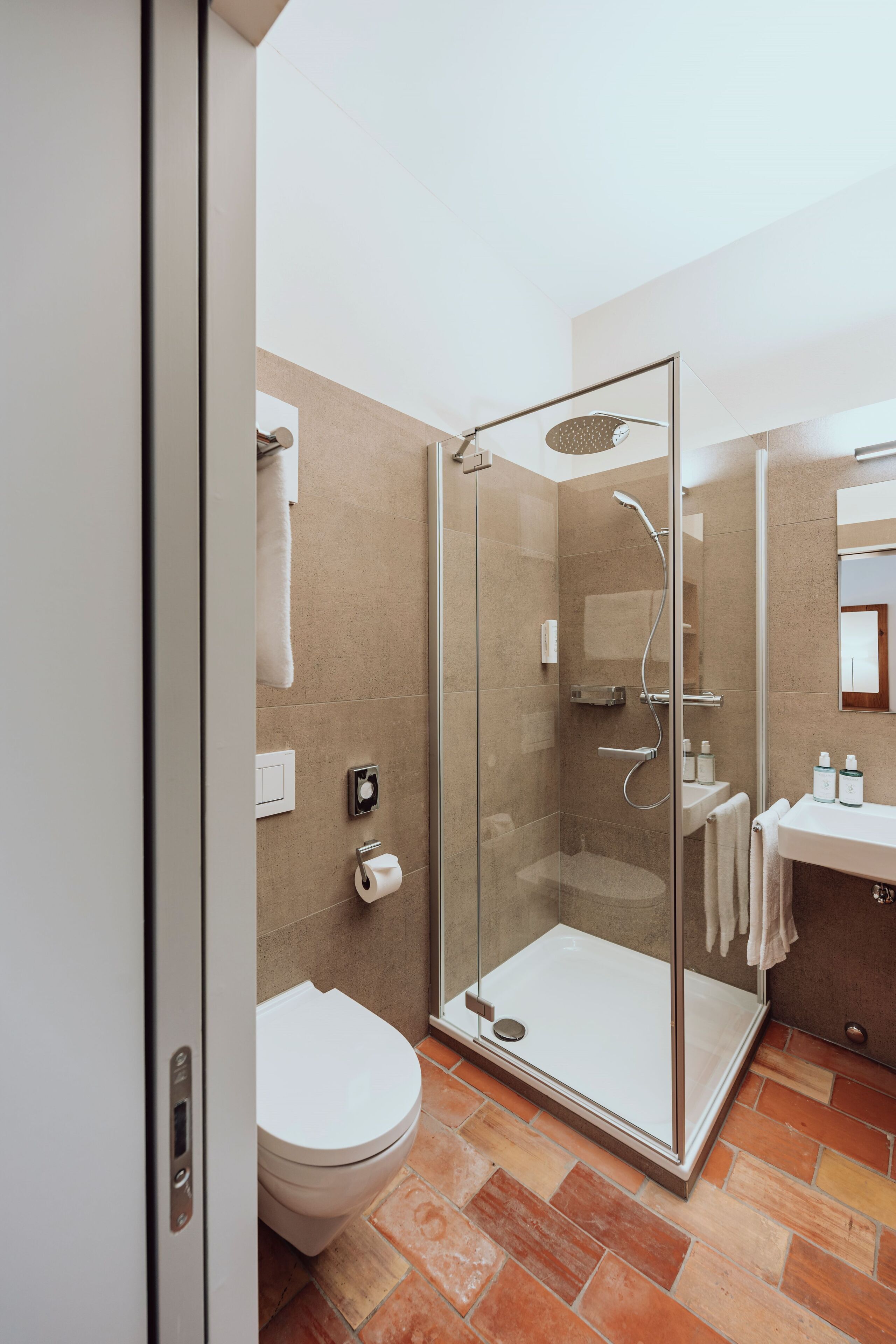 A modern bathroom with a glass-enclosed shower, a white toilet, and a sink area.