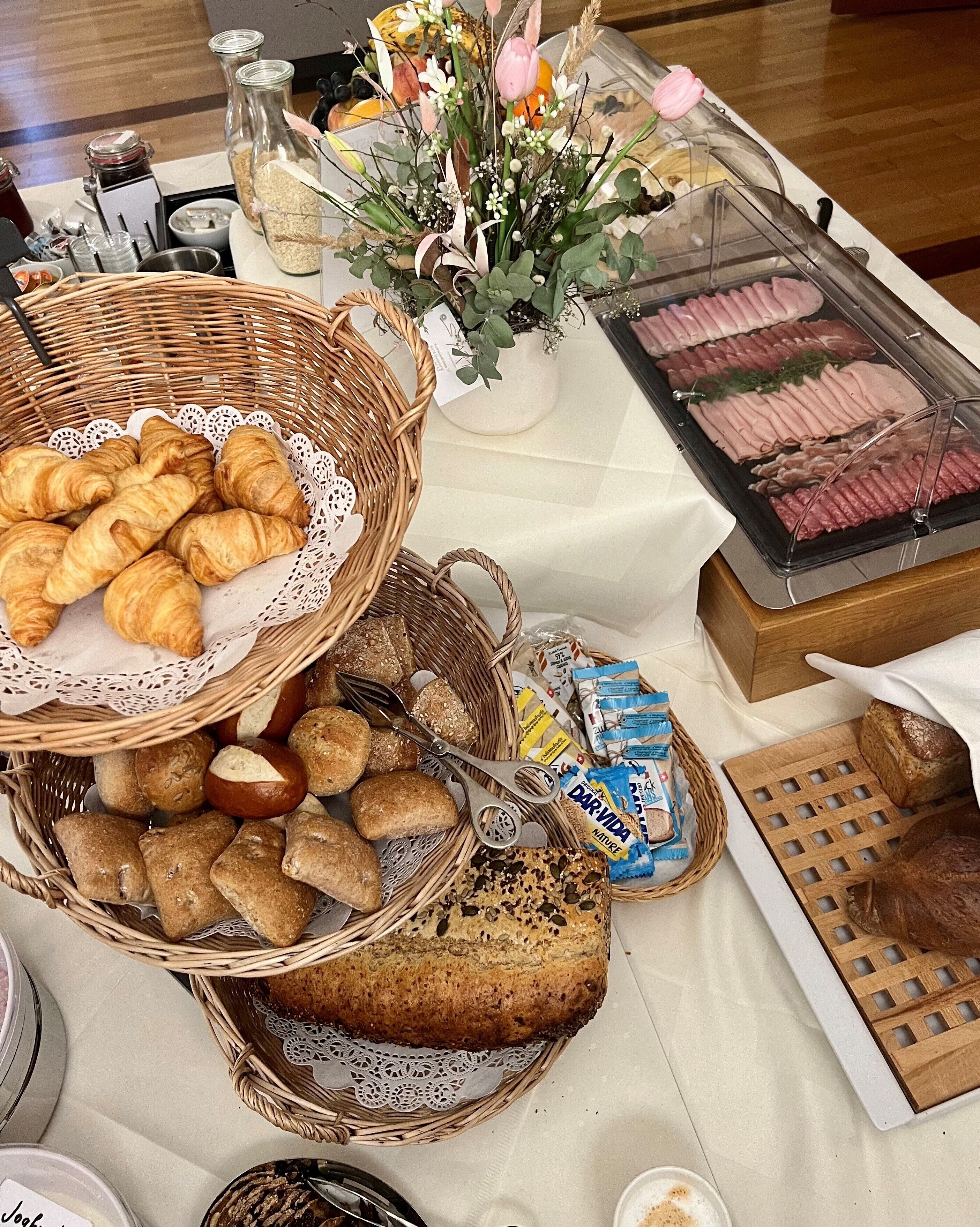 A buffet table with various food items including bread, pastries, and meat.