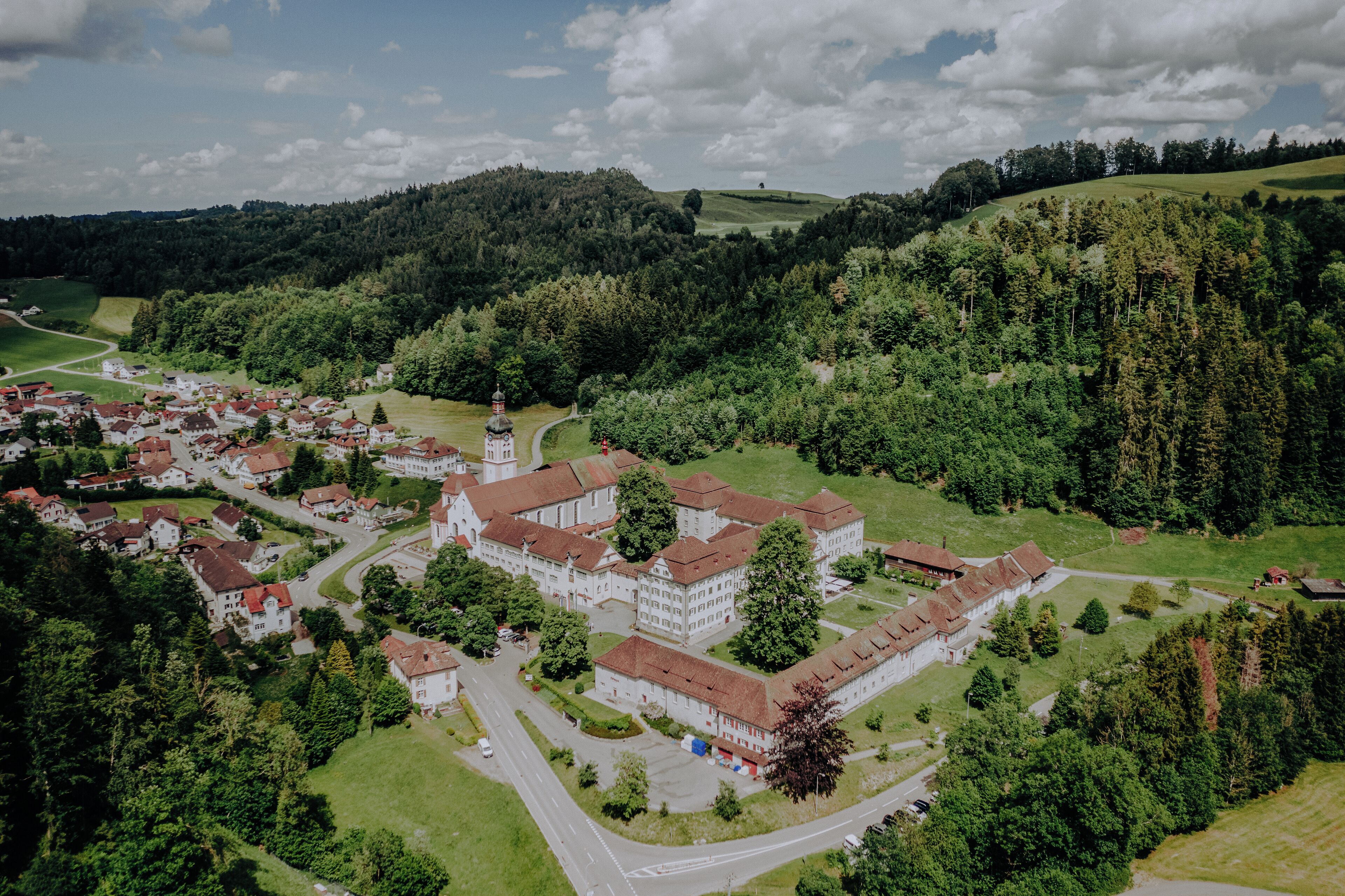 An aerial view of a village with a prominent building complex surrounded by greenery and a few houses.