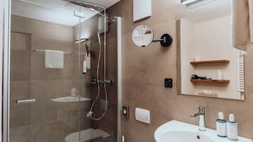 Een moderne badkamer met een douche met glazen wand, een witte wastafel en een spiegel erboven.