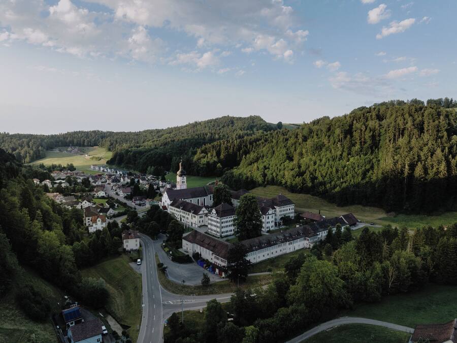 An aerial view of a town with a prominent church, surrounded by lush green hills and a clear sky.