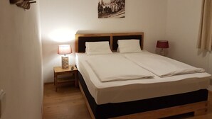 A neatly made bed with white linens, a wooden headboard, and two bedside lamps. - Sportpension Penhab (Saalbach-Hinterglemm)