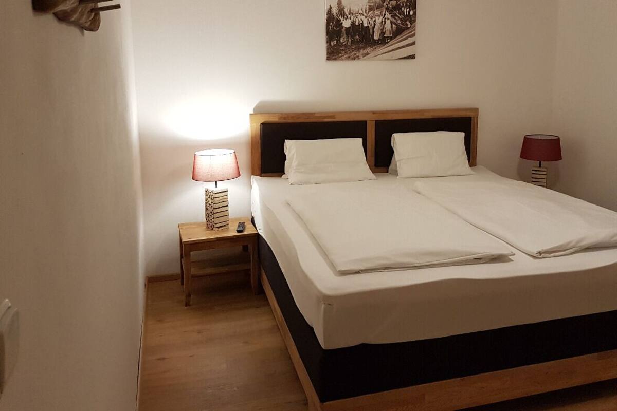 Un lit bien fait, avec du linge de lit blanc, une tête de lit en bois et deux lampes de chevet.