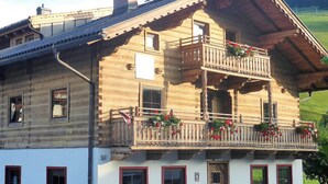 A wooden chalet with a balcony adorned with flowers, a mountain backdrop, and a traditional Alpine architectural style. - Sportpension Penhab (Saalbach-Hinterglemm)