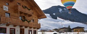 Un chalet en bois doté de balcons, une piste de ski en arrière-plan et une montgolfière.