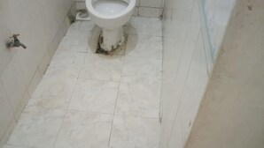A bathroom with a toilet, a drain, and a pair of red slippers on the floor. - Jambo Guest House (Gilgil)