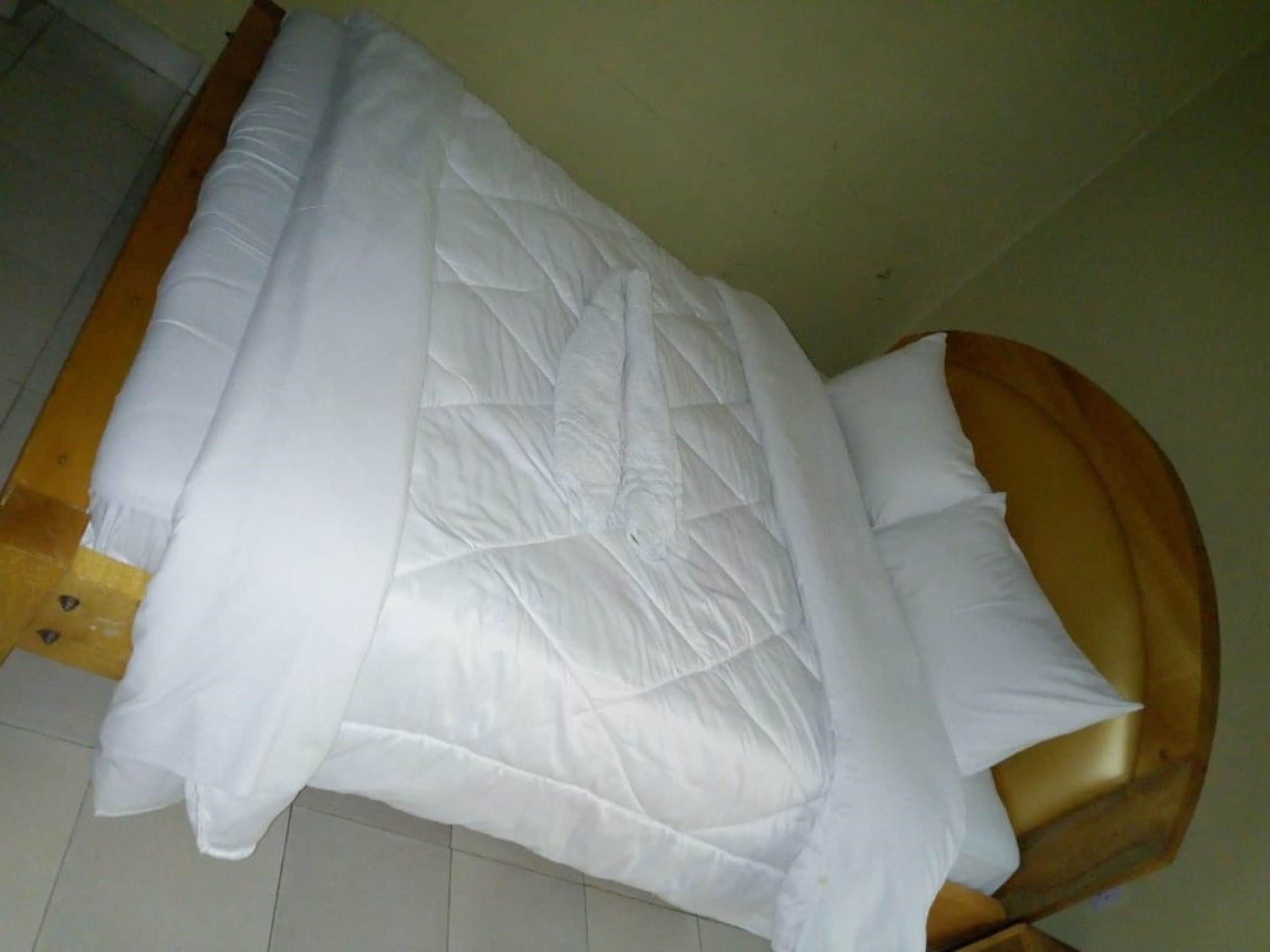 Una cama con edredón blanco acolchado y cabecera de madera.