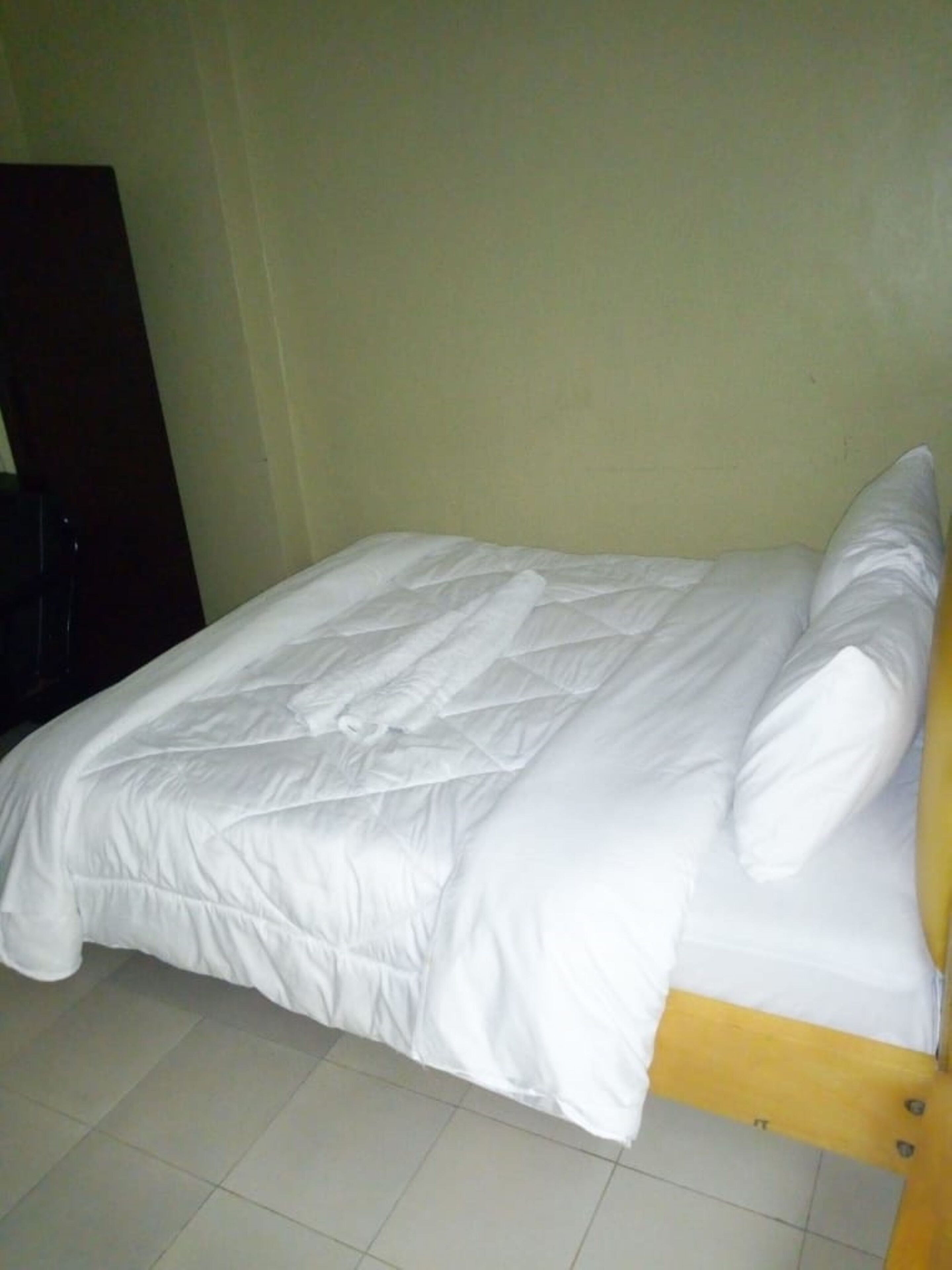A bed with white bedding in a room with plain walls and a tiled floor.
