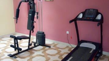 A home gym with a treadmill, weight bench, and cable machine.