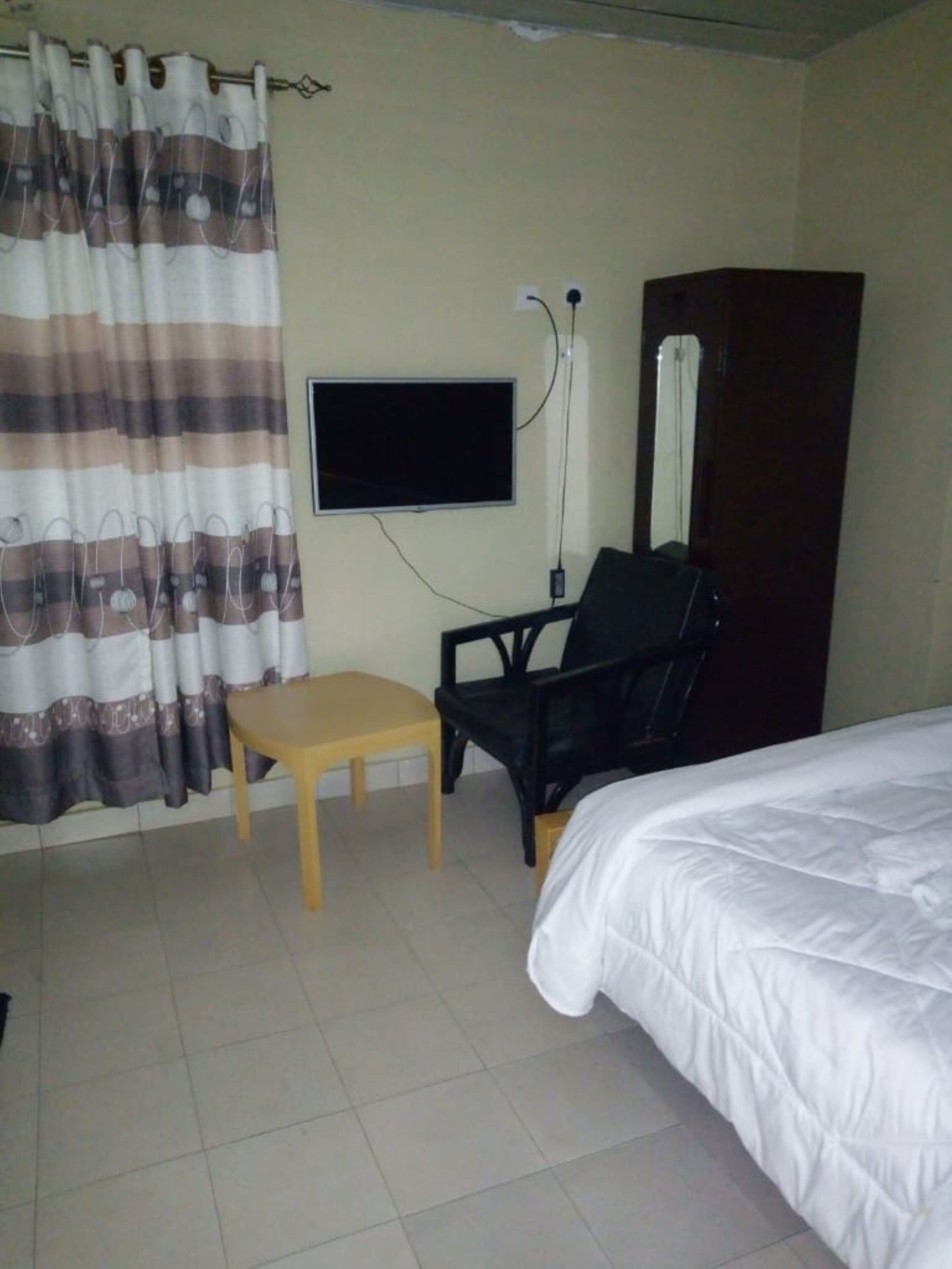 Una habitación de hotel con una cama, televisión montada en la pared, una silla y una pequeña mesa.