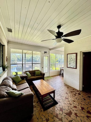 Relax in this spacious living area with a high ceiling and ceiling fan. Enjoy the view from the large window and unwind on the comfortable sofa.
