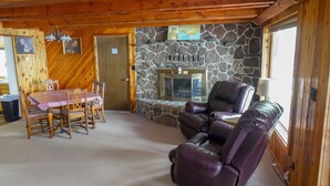 A cozy living room with a stone fireplace, wooden furniture, and a dining area with a checkered tablecloth. - The west shore getaway on Canyon Ferry. (Helena)