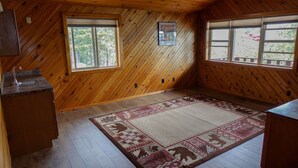A room with wooden walls, a kitchen area with a sink, two windows, and a patterned rug. - The west shore getaway on Canyon Ferry. (Helena)