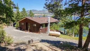 A cabin with a wooden exterior, a gravel driveway, and a view of a lake and mountains in the background. - The west shore getaway on Canyon Ferry. (Helena)
