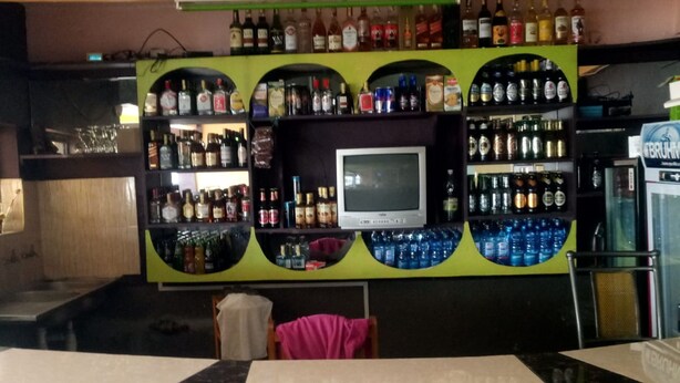 A bar area with shelves of liquor bottles, a television, and a refrigerator. - Romani Resort (Nakuru)
