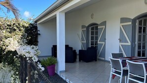 Un patio couvert doté d’une balustrade blanche, d’une table avec des chaises et d’une porte ornée de motifs géométriques.