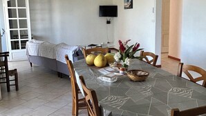 Un coin repas avec une table dressée pour quatre personnes, un ventilateur de plafond, un téléviseur fixé au mur et une porte donnant sur une autre pièce.