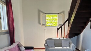Huoneessa on kaksi sohvaa, ikkuna, josta on näkymä vehreään maisemaan, ja portaikko.