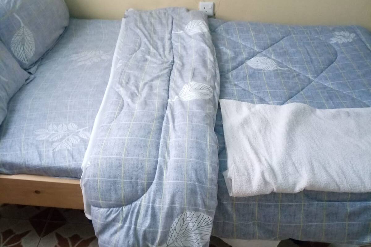 A bed with a blue and white patterned bedspread and pillows, a wooden headboard, and a tiled floor with a geometric pattern.