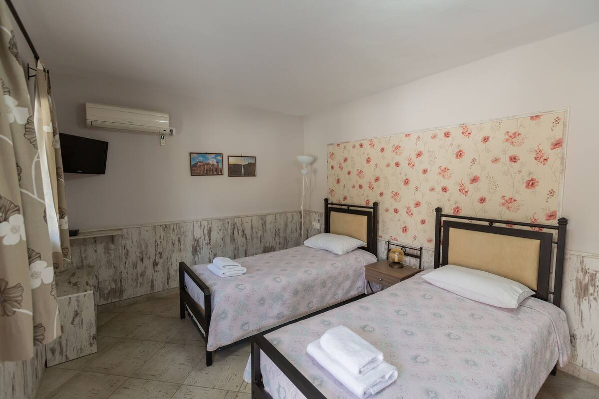 Ein Zimmer mit zwei Einzelbetten, einem flachbildfernseher an der Wand und einem Deckenventilator.