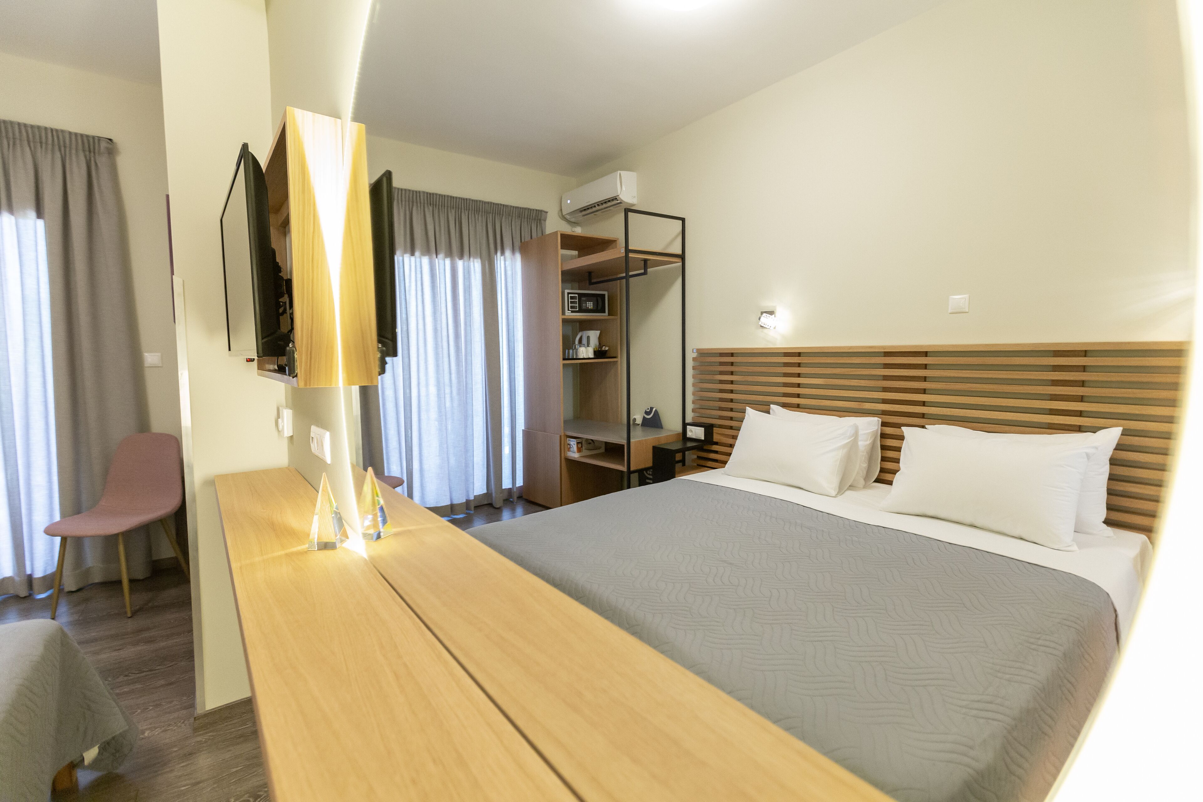 Una habitación de hotel con cama, mesita de noche, lámpara, silla y escritorio con computadora y estanterías.