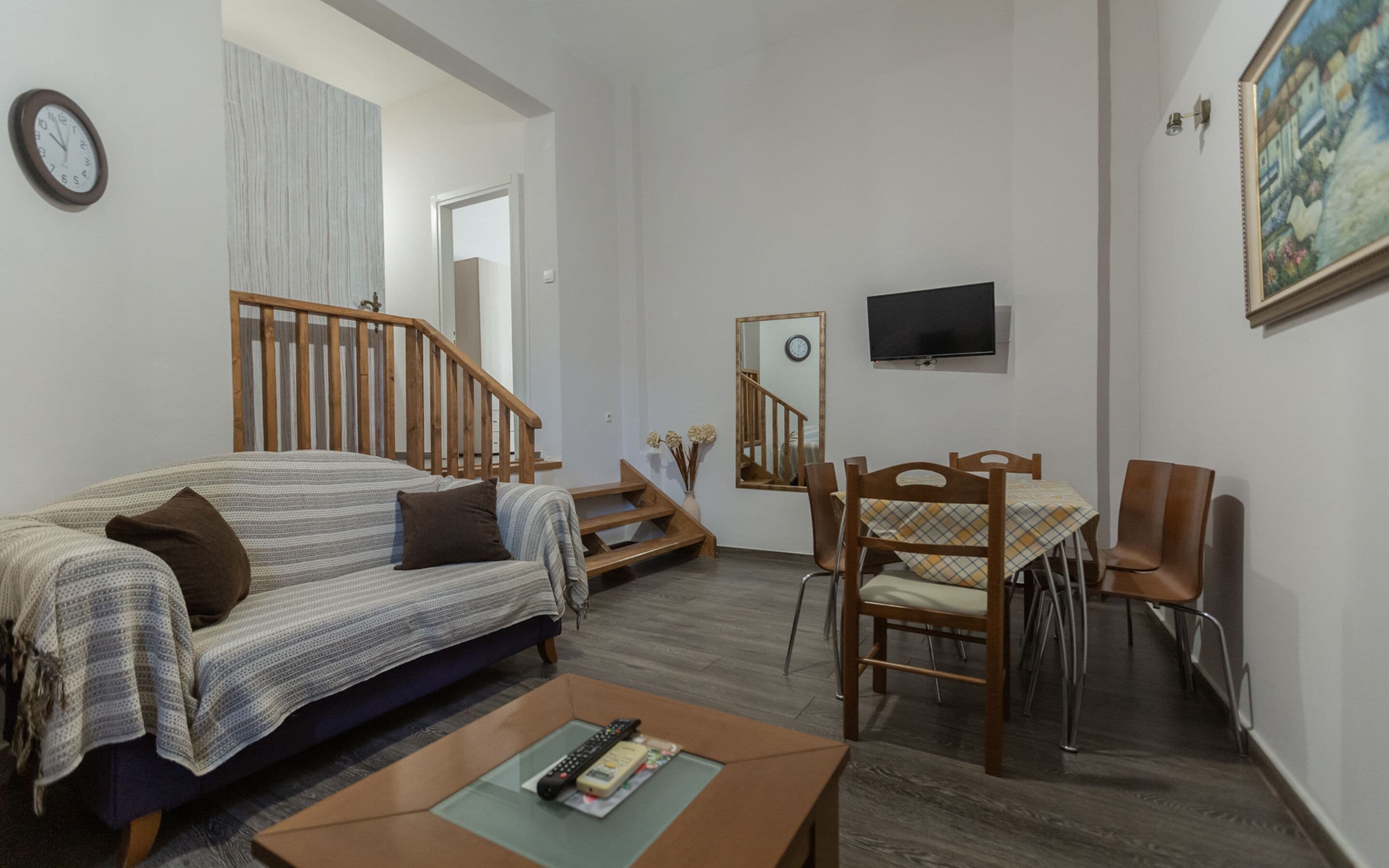 Ein Wohnzimmer mit einer Couch, einem Couchtisch, einem Fernseher, einem Esstisch mit Stühlen und einer Treppe.