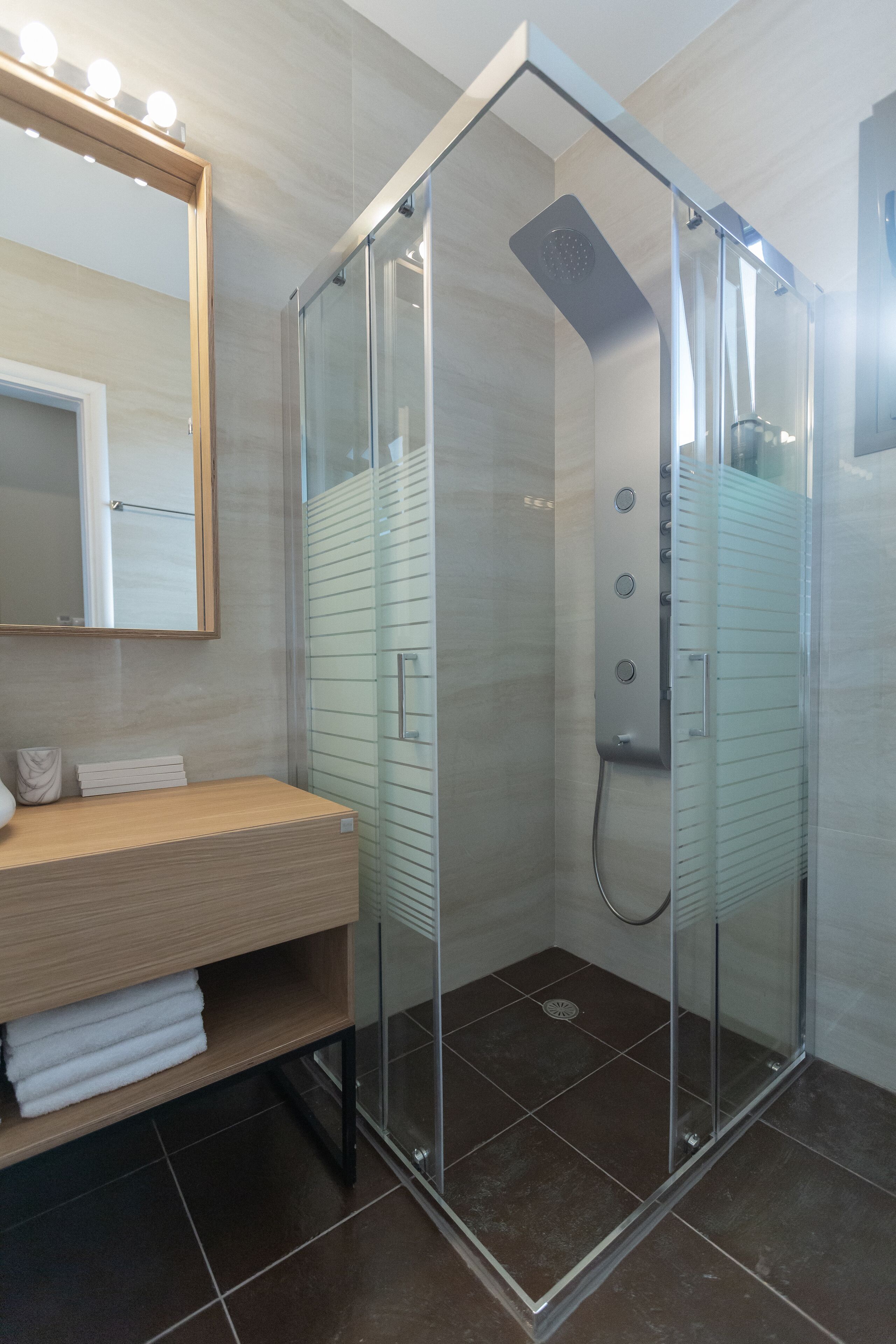 Une salle de bain moderne avec une douche à parois de verre, un meuble-lavabo en bois et un miroir avec éclairage intégré.