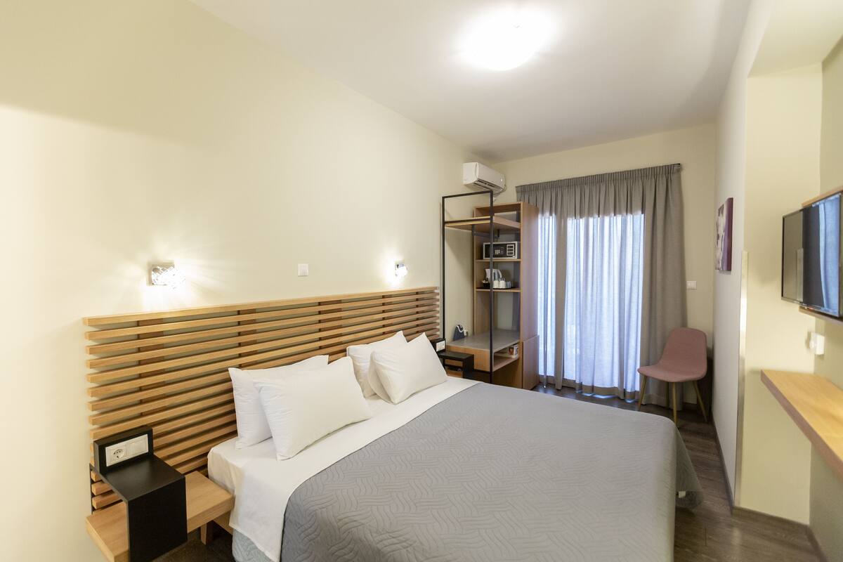 Ein Hotelzimmer mit Bett, Nachttischen, Fernseher, Sessel und einem Regal mit Gegenständen.