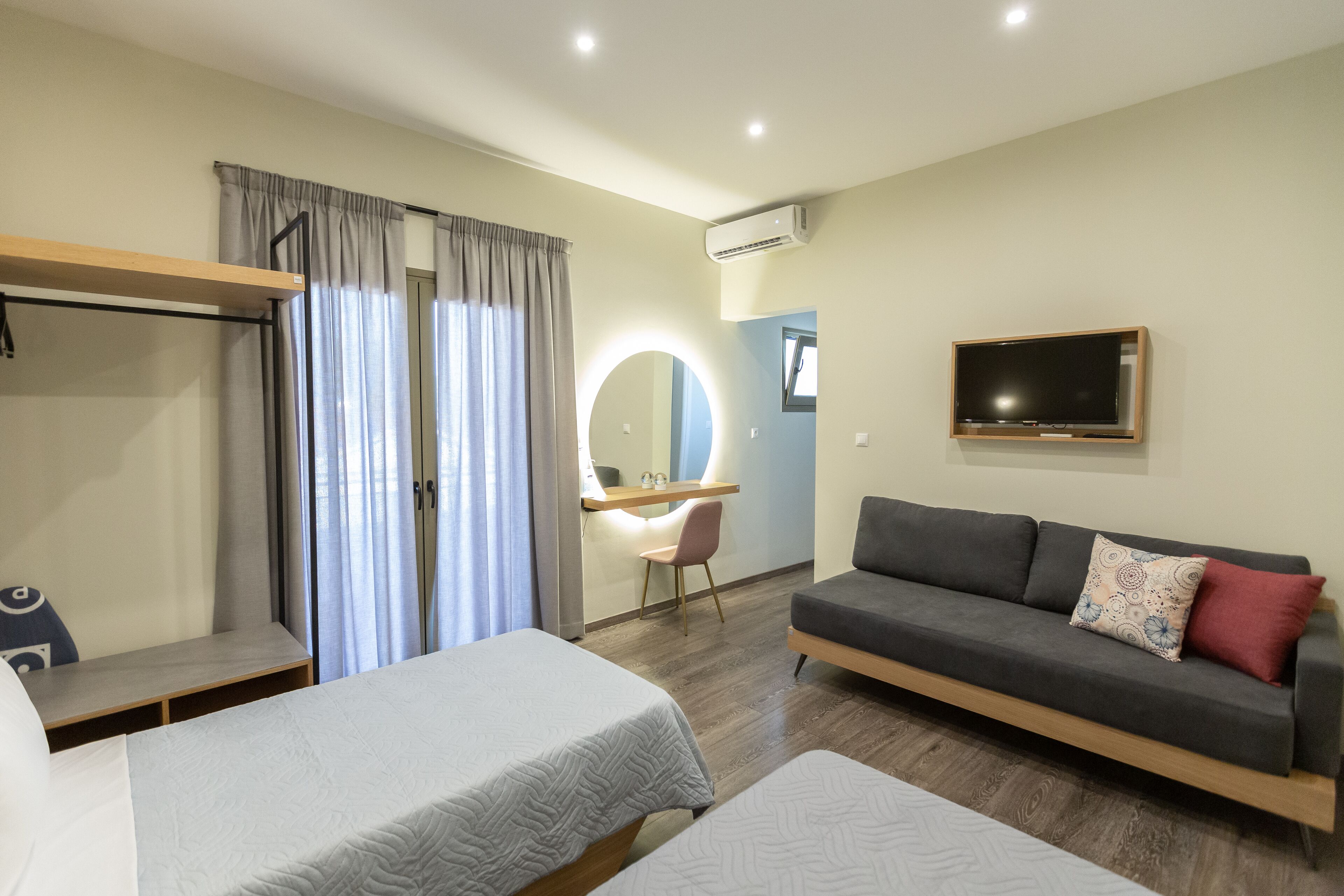 A hotel room with two beds, a desk, a sofa, a TV, and an air conditioning unit.