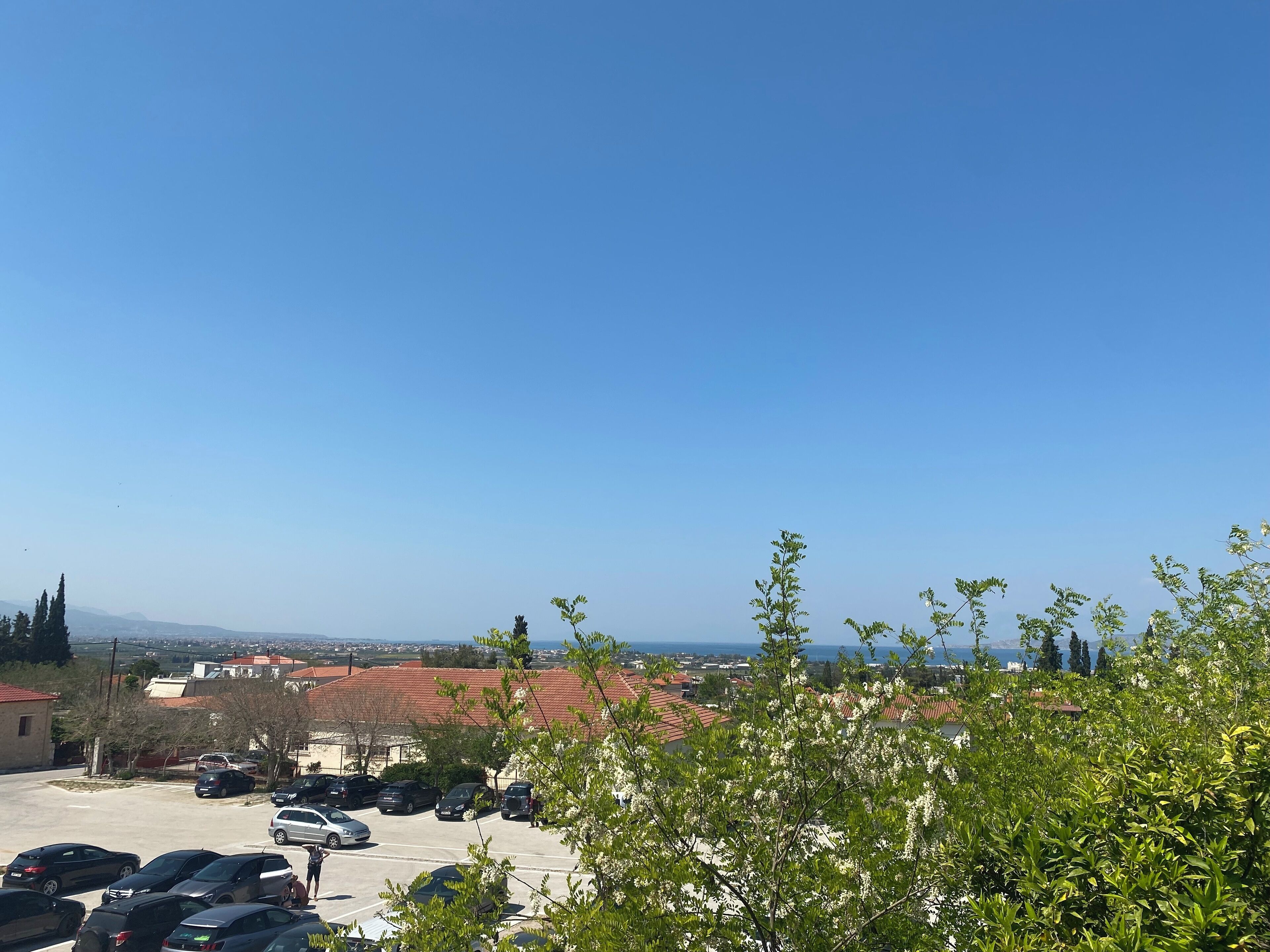 A parking lot with several cars, a building with red roofs, and a clear blue sky.