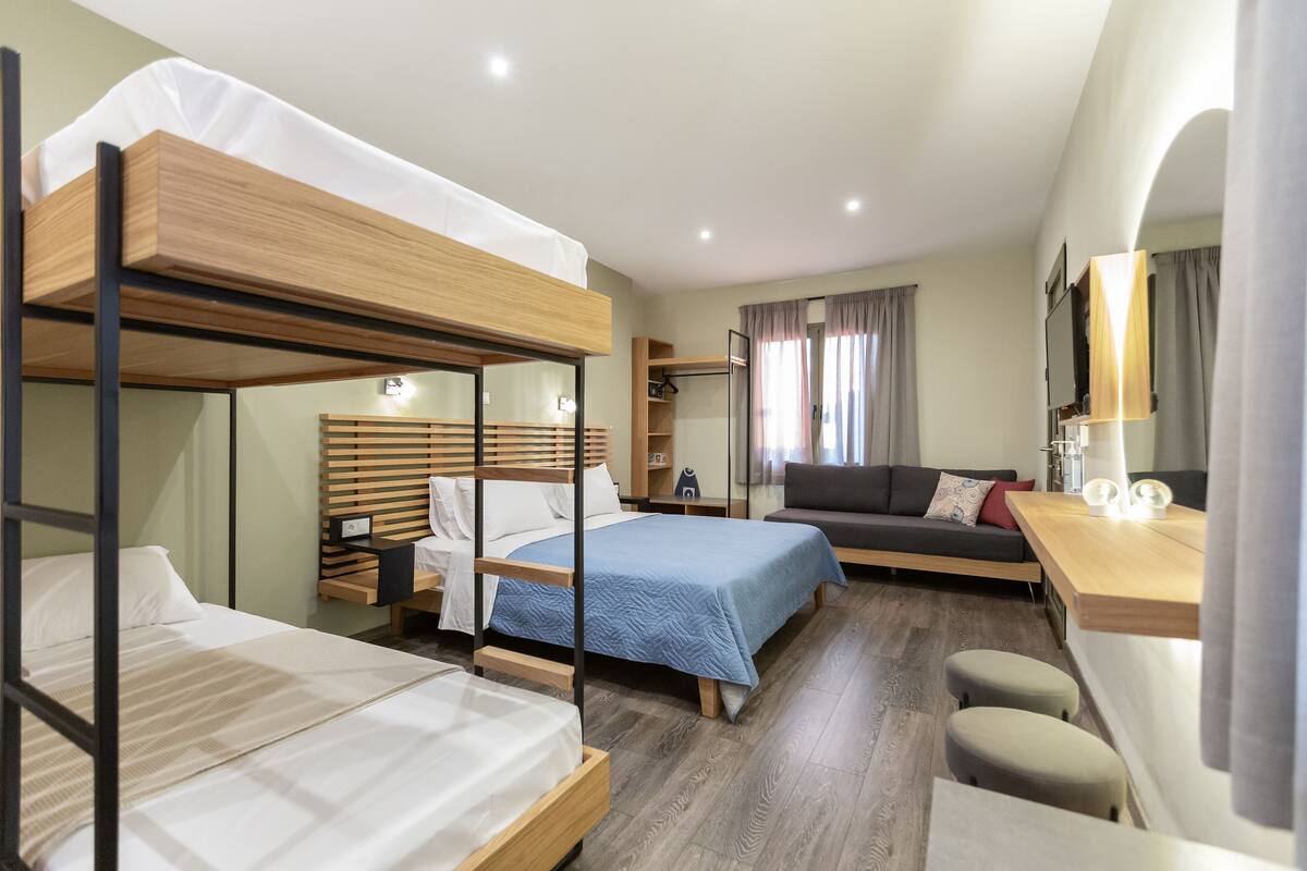 Ein kleines Hotelzimmer mit Etagenbetten, einer Schlafcouch, einem Schreibtisch und einem Fernseher.