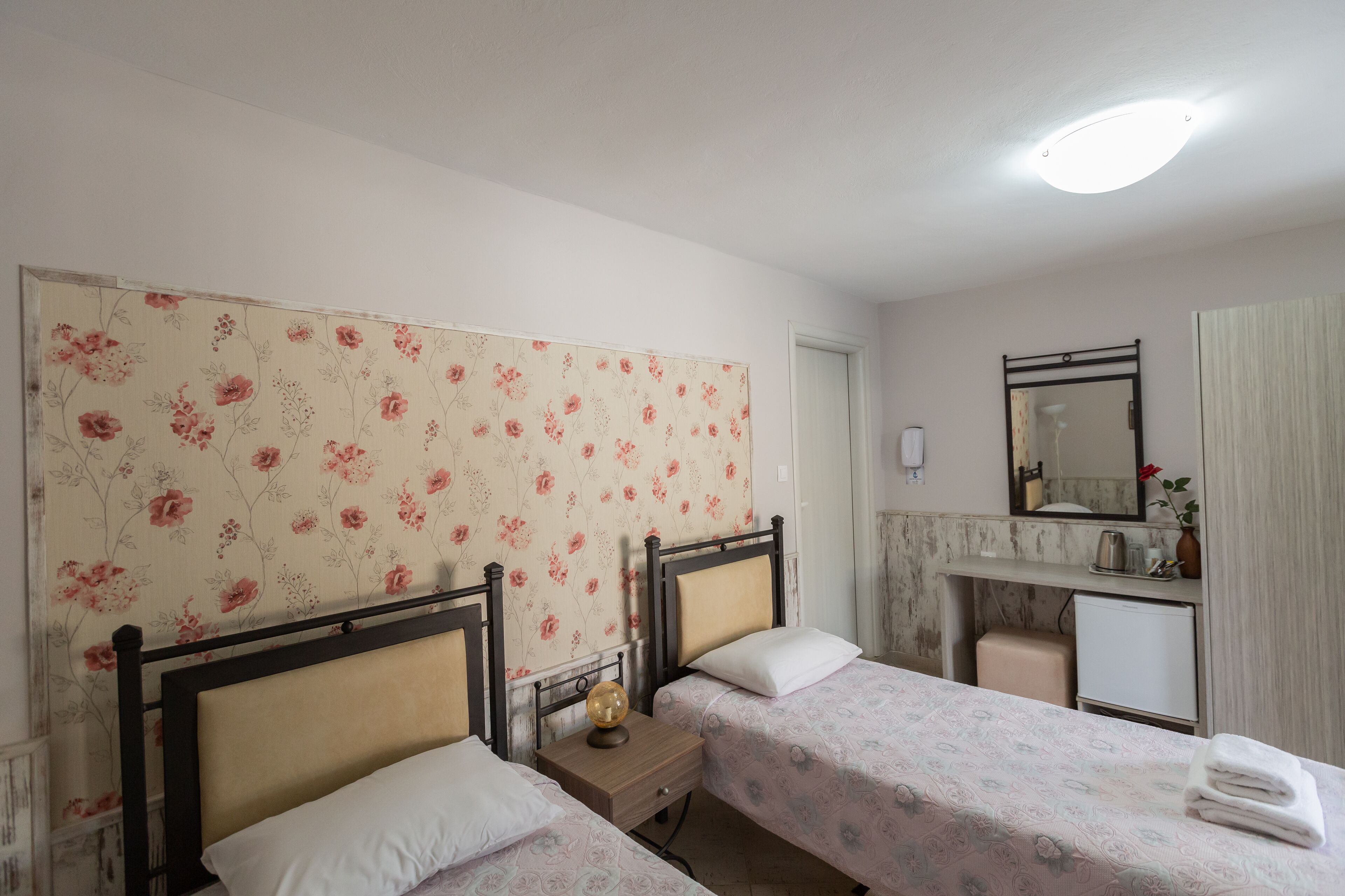 A bedroom with two beds, a nightstand, a dresser, a mirror, and a small desk with a lamp.