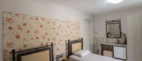 A bedroom with two beds, a nightstand, a dresser, a mirror, and a small desk with a lamp.