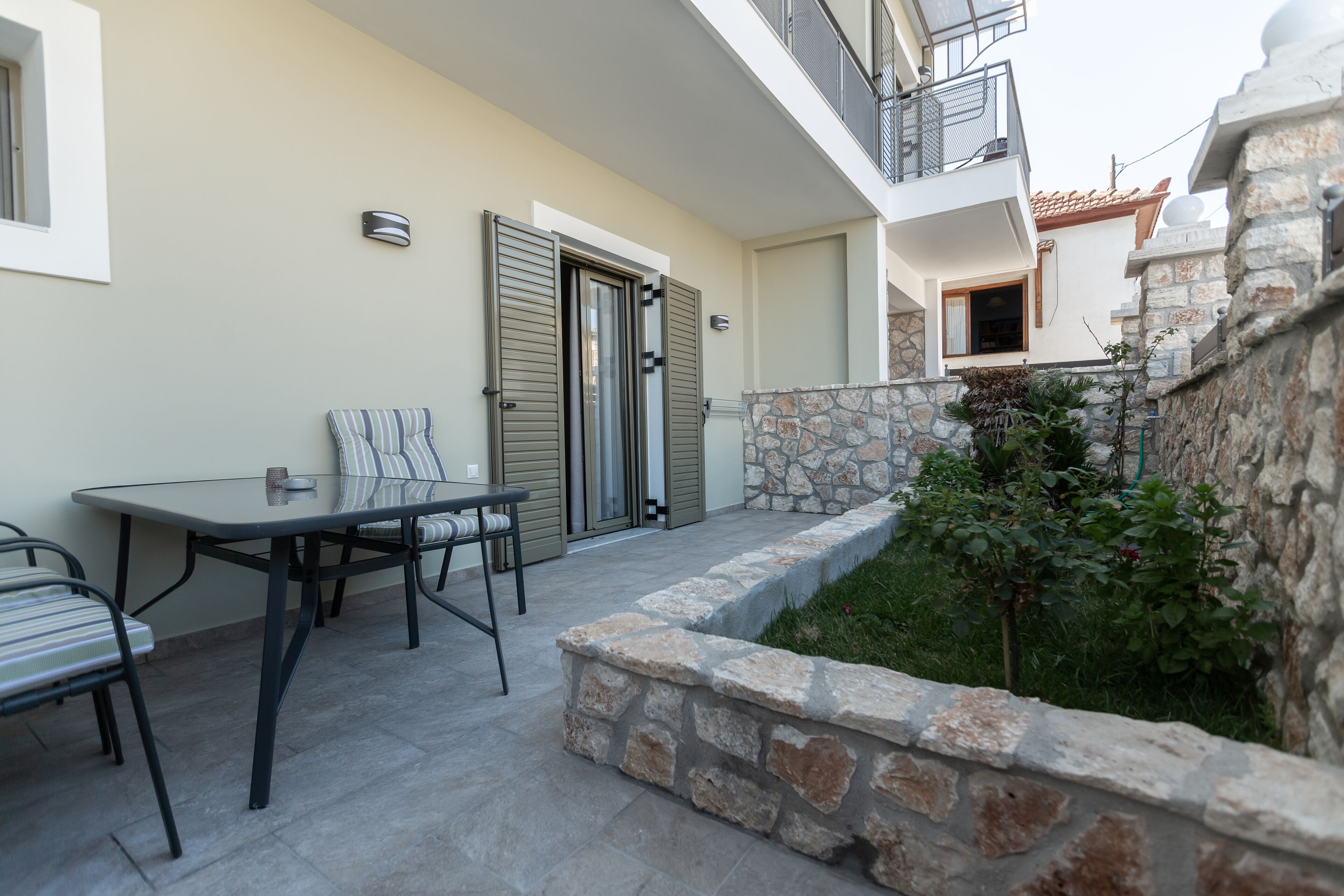 An outdoor patio with a table and chairs, a stone wall, and a door.