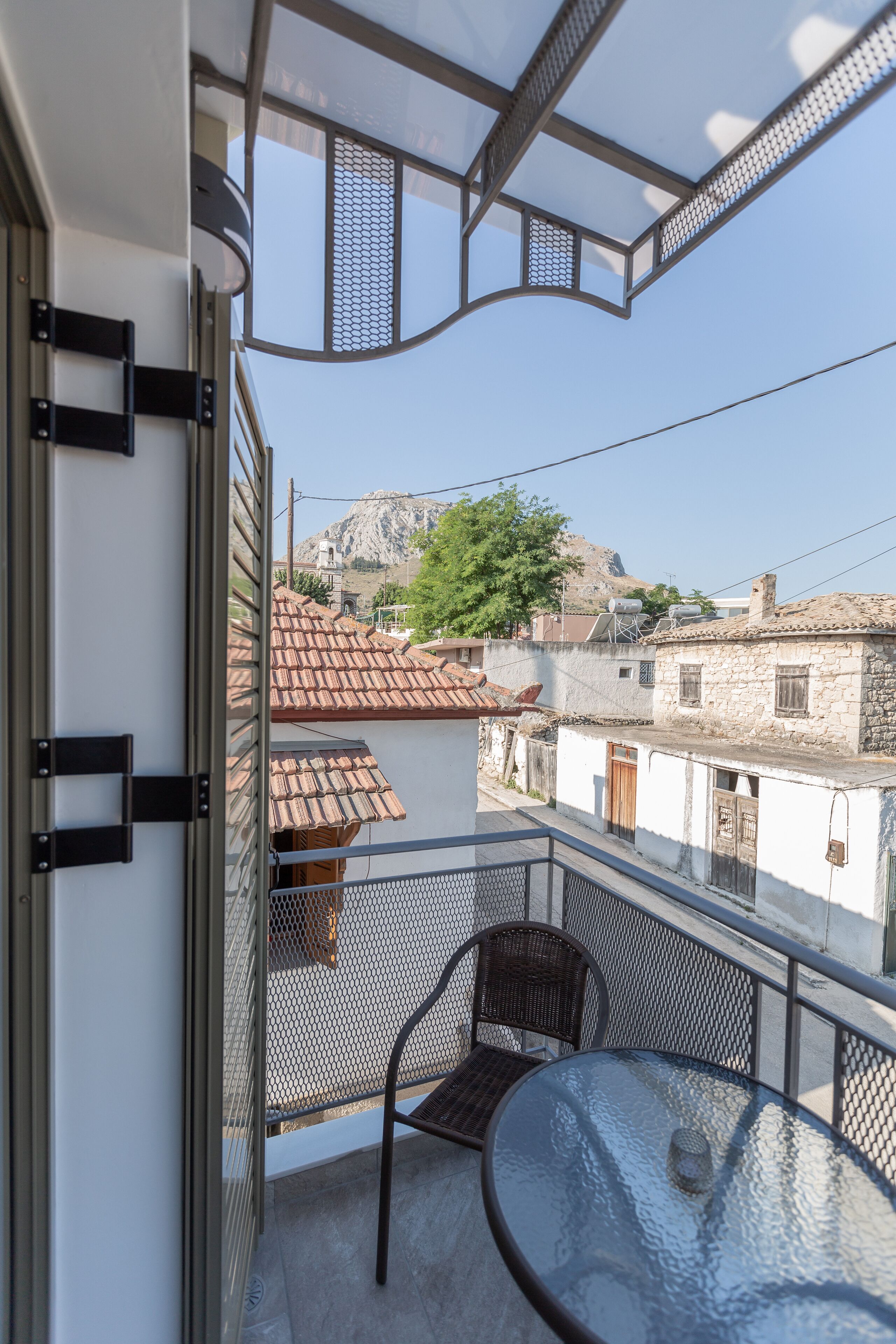 Un balcon avec une table et des chaises en verre, donnant sur une ville aux bâtiments traditionnels et surmontée d’une montagne en arrière-plan.