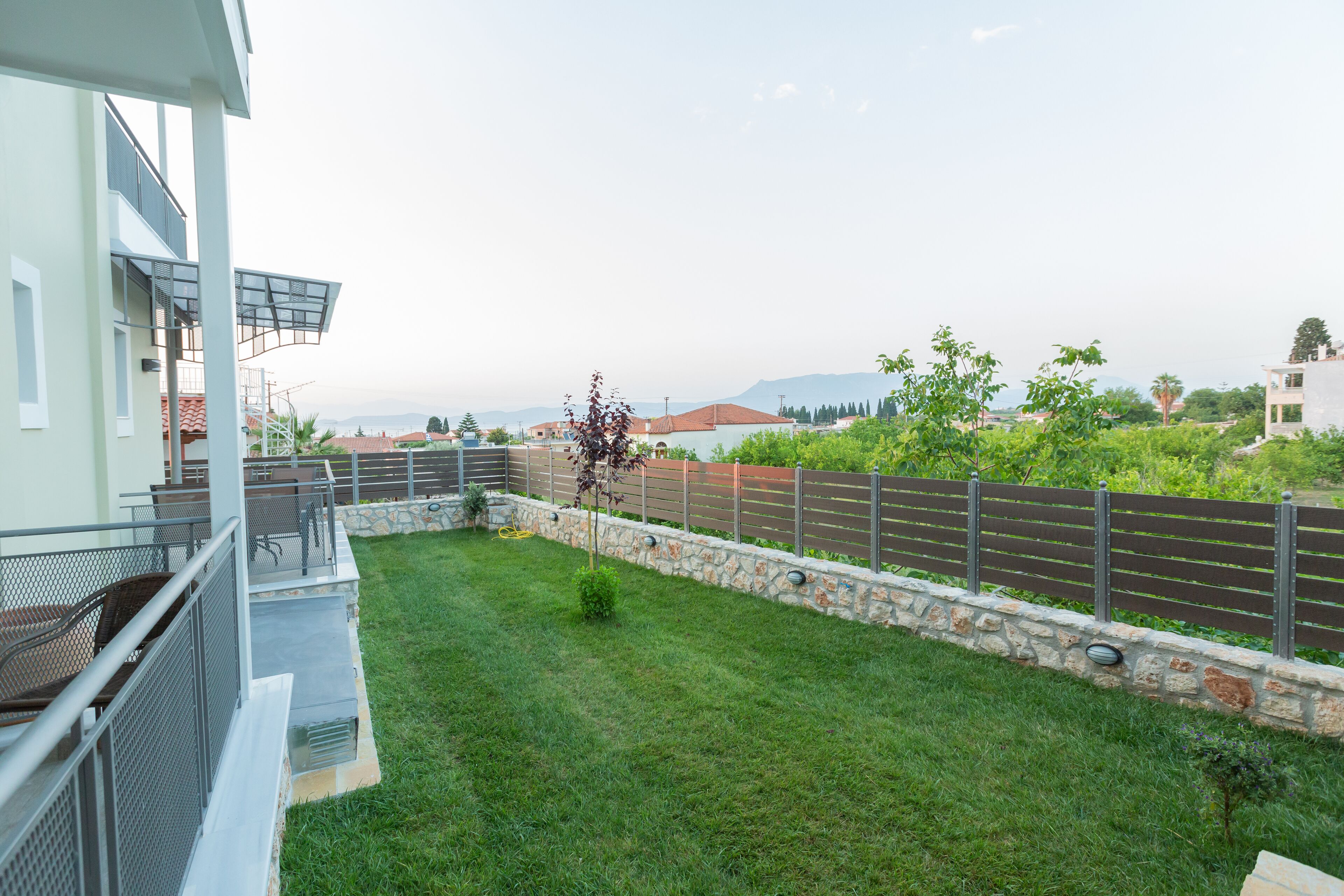 A residential property with a stone retaining wall, a grassy backyard, and a balcony with metal railings.