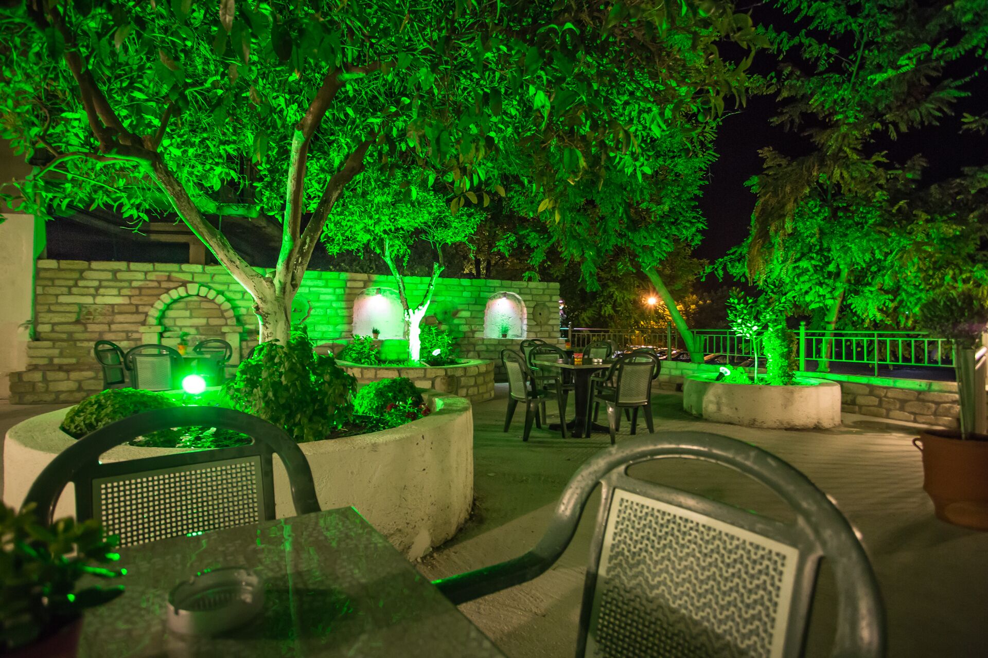 An outdoor seating area with tables and chairs, surrounded by greenery and stone walls.