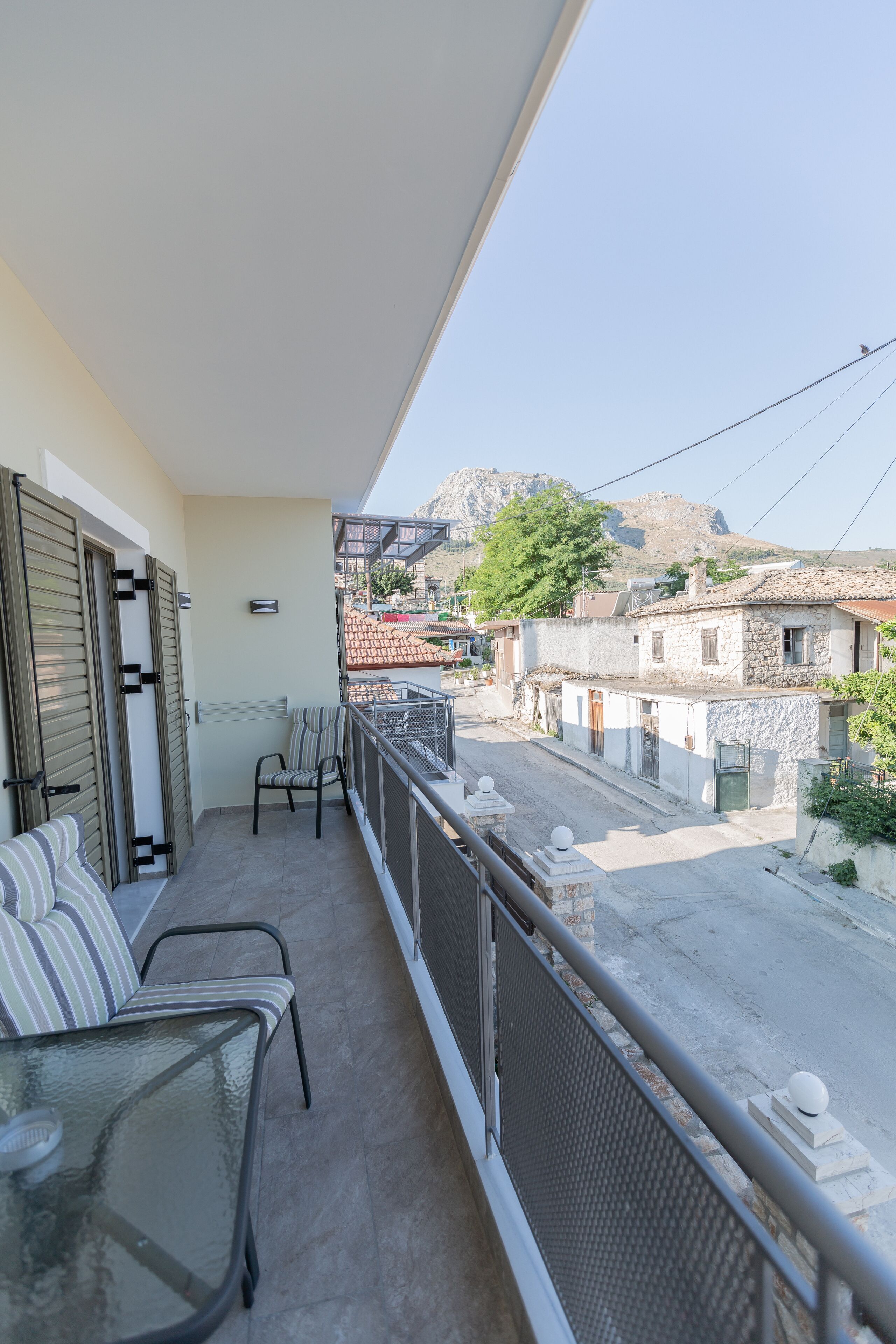 Ein Balkon mit einer Couch und Stühlen, Blick auf eine Straße und Gebäude, und ein Berg in der Ferne.