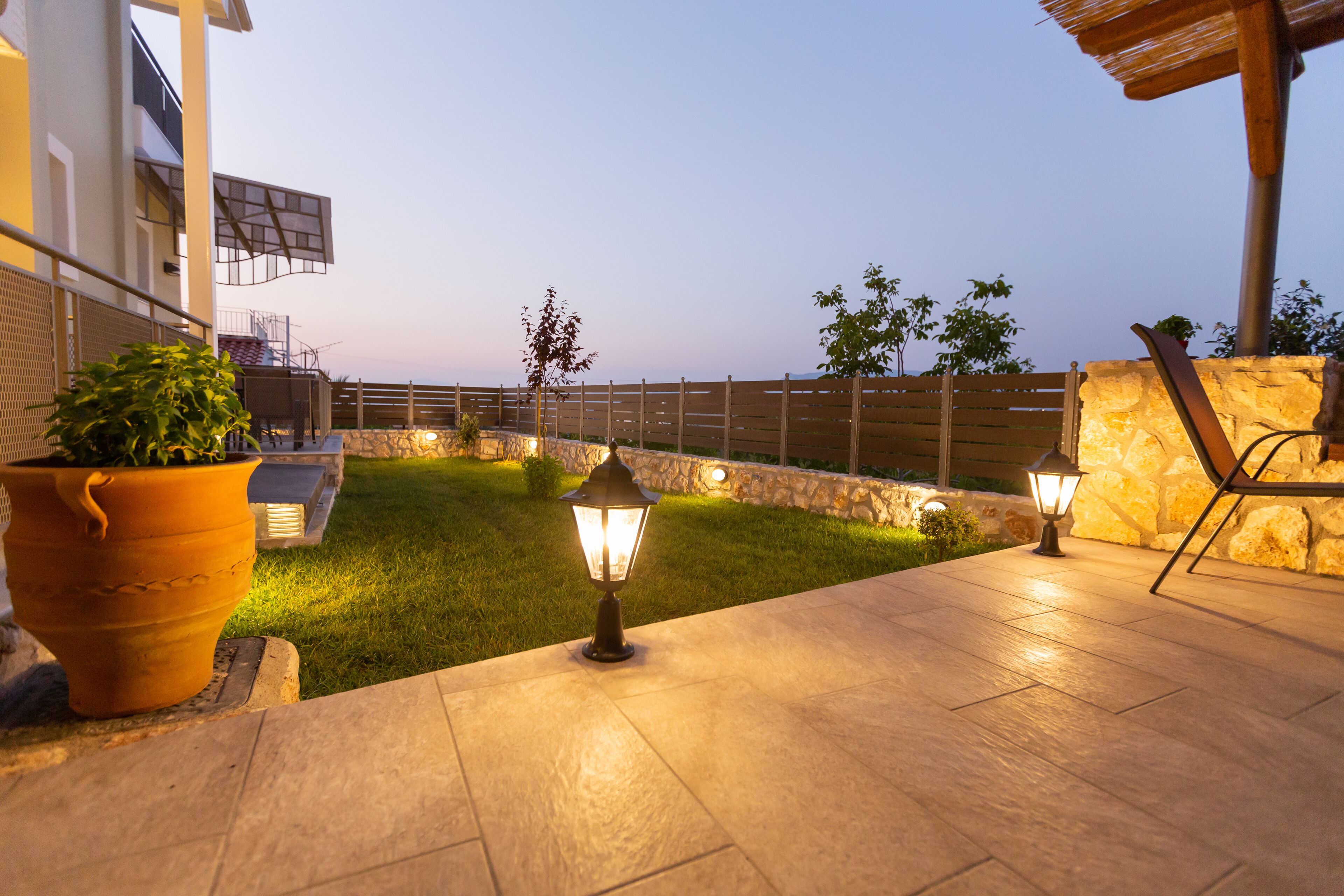 Ein Terrassenbereich im Freien mit Steinboden, zwei Kübelpflanzen und zwei Wandleuchtern.